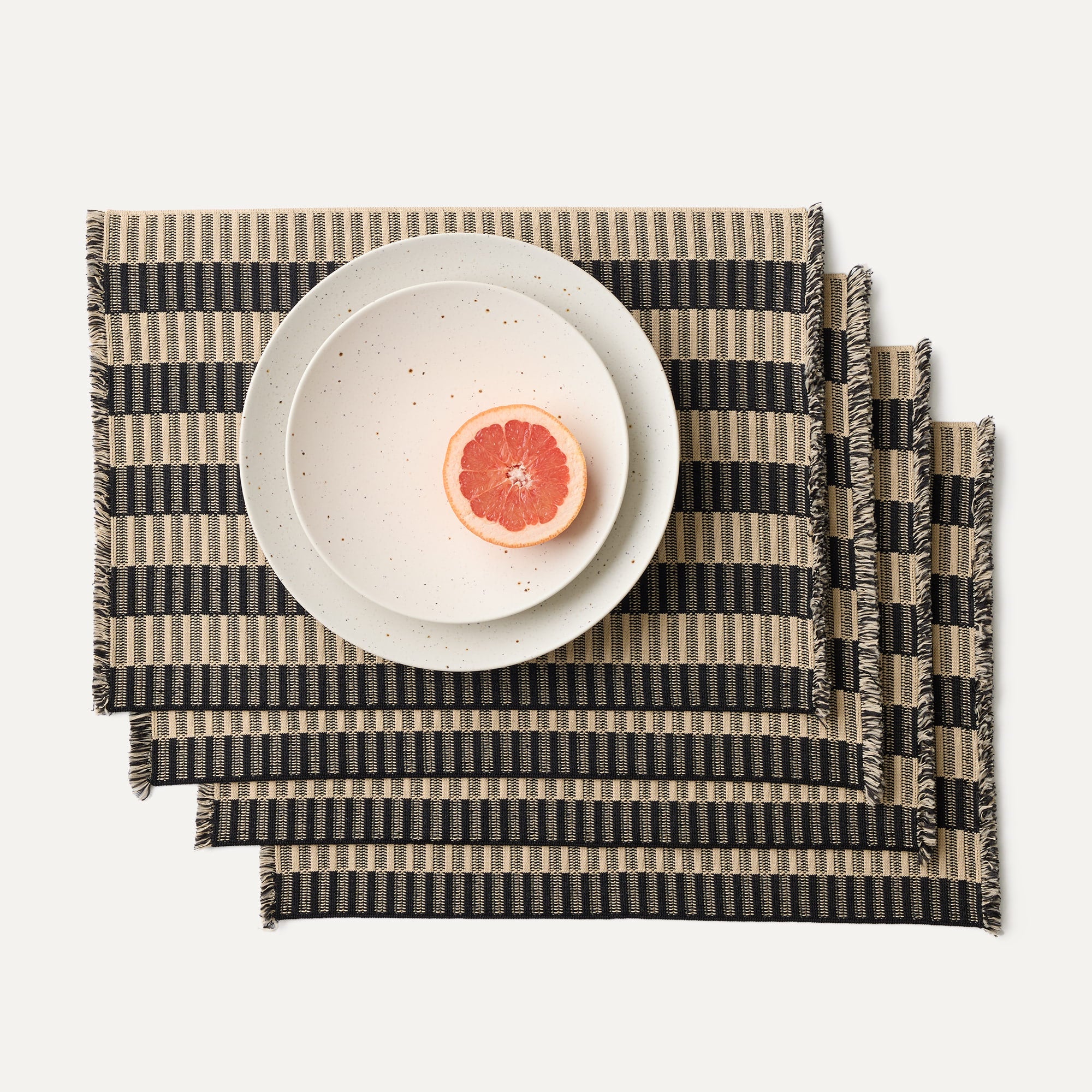 A set of four Placemats in Peppercorn Fringe shown with a plate setting.